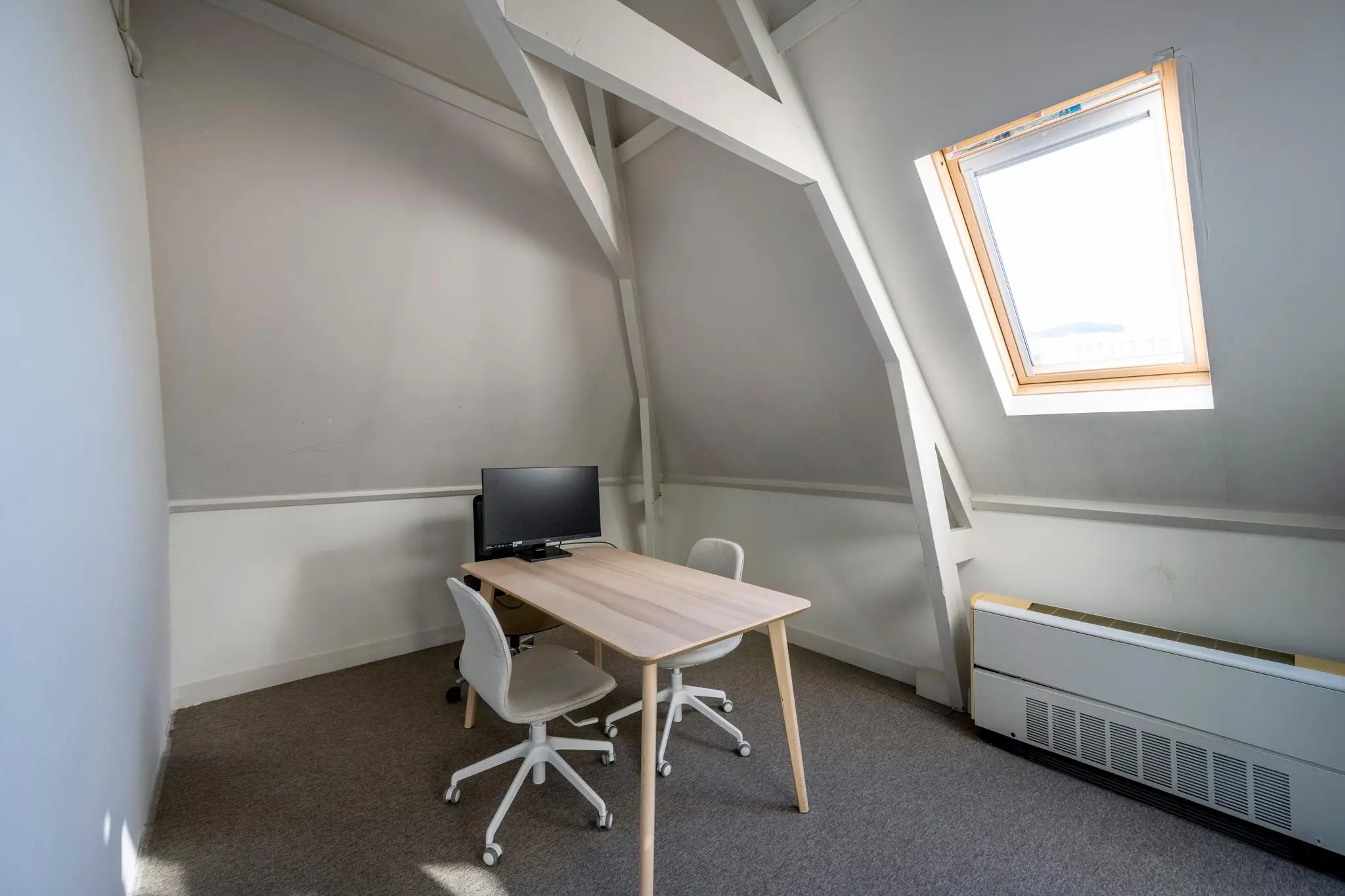 Kleine kantoorruimte aan de Prof. Tulpstraat met schuin dak, twee stoelen, een bureau en een computerscherm.